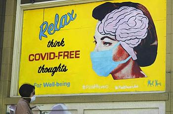 A woman wears a face mask while walking under a sign that reads "Relax think COVID free thoughts" during the coronavirus outbrea